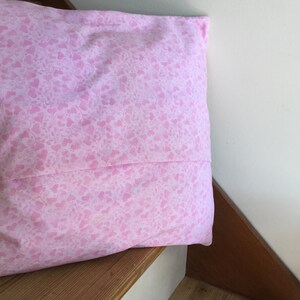 May include: A pink pillow with a white heart pattern. The pillow is on a wooden surface.
