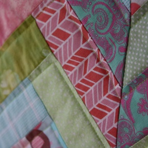 May include: A close-up of a patchwork quilt with a chevron pattern. The quilt is made of various fabrics in shades of pink, green, and blue.