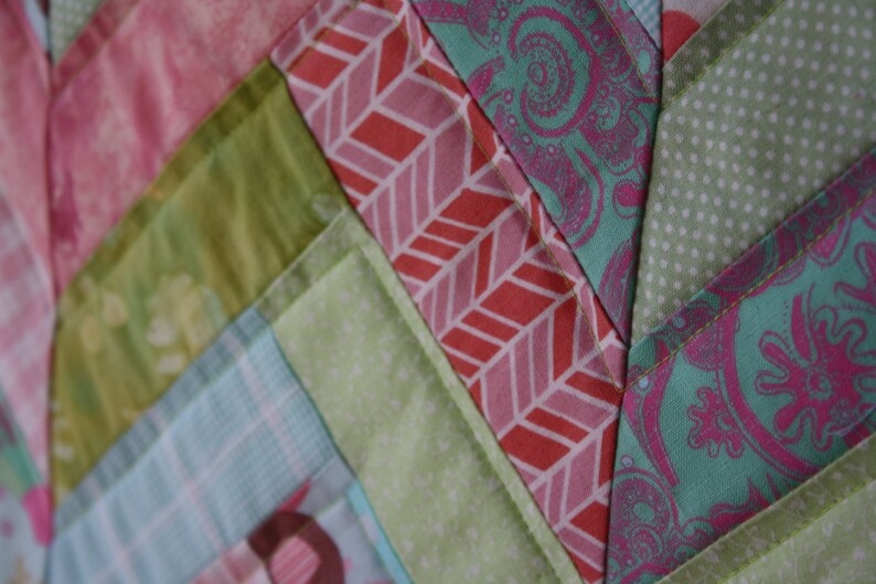 May include: A close-up of a patchwork quilt with a chevron pattern. The quilt is made of various fabrics in shades of pink, green, and blue.