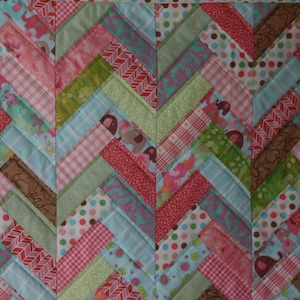 May include: A patchwork quilt with a chevron pattern in shades of pink, green, blue, and brown. The quilt is made of various fabrics with different patterns, including polka dots, stripes, and floral prints.