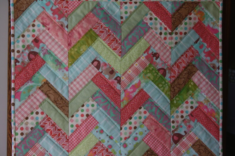 May include: A patchwork quilt with a chevron pattern in shades of pink, green, blue, and brown. The quilt is made of various fabrics with different patterns, including polka dots, stripes, and floral prints.