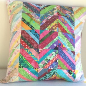 May include: A colorful patchwork pillow with a chevron pattern. The pillow is made from a variety of fabrics in shades of pink, green, blue, yellow, and red.