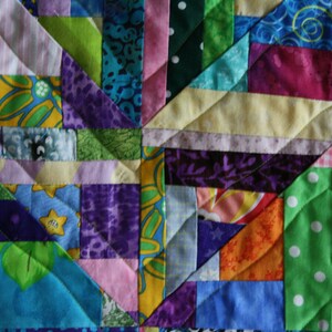 May include: A colourful patchwork quilt featuring a range of fabrics and patterns, including floral, geometric, and polka dot designs. The quilt is made up of squares and triangles, and the colours are bright and vibrant.