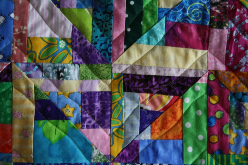 May include: A colourful patchwork quilt featuring a range of fabrics and patterns, including floral, geometric, and polka dot designs. The quilt is made up of squares and triangles, and the colours are bright and vibrant.