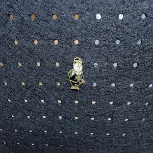 May include: A gold-toned metal enamel pin featuring a cartoon character wearing a hat and a suit with a star emblem on the chest. The character has a white face with black facial features and is depicted in a standing pose with arms at the sides.