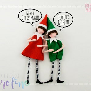 Puede incluir: Dos muñecas de duendes con atuendos rojo y verde y medias rayadas en blanco y negro. El duende de la izquierda sostiene un globo de diálogo que dice "Merry Christmas!!!" y el duende de la derecha sostiene un globo de diálogo que dice "Joyeux Noel!!!".