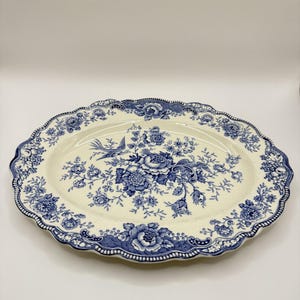 May include: An oval ceramic serving platter featuring a cream-colored base with a detailed blue floral and bird pattern. The rim has a scalloped edge with a decorative blue border. The central design displays intricate flowers and a bird in flight.