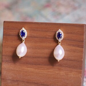 May include: A pair of gold earrings with a blue gemstone surrounded by clear stones and a white pearl drop.