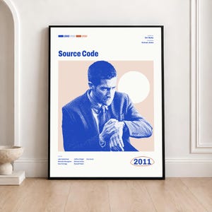 Op de afbeelding: Een ingelijste filmposter voor Source Code met een blauw getinte illustratie van een persoon in een blazer die op een horloge kijkt. Het ontwerp bevat de tekst Source Code, 2011 en credits voor Ben Ripley, Duncan Jones en de cast.