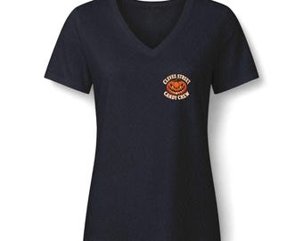 May include: A dark navy blue V-neck t-shirt featuring a small circular graphic on the left chest. The graphic displays an orange jack-o'-lantern with a sinister expression and the text Cleves Street Candy Crew in a curved font.