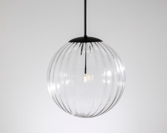 May include: A clear glass globe pendant light with a black cord and a black metal canopy. The globe has a ribbed texture.