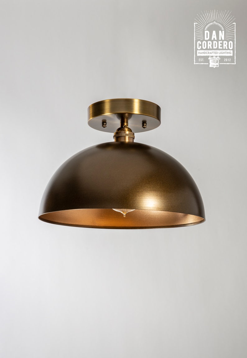 May include: A brass dome ceiling light fixture with a gold interior. The light fixture is mounted on a white ceiling.