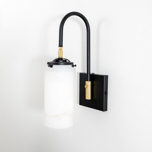 May include: Black wall sconce with a white alabaster glass shade and gold accents. The sconce has a curved arm and a square base.