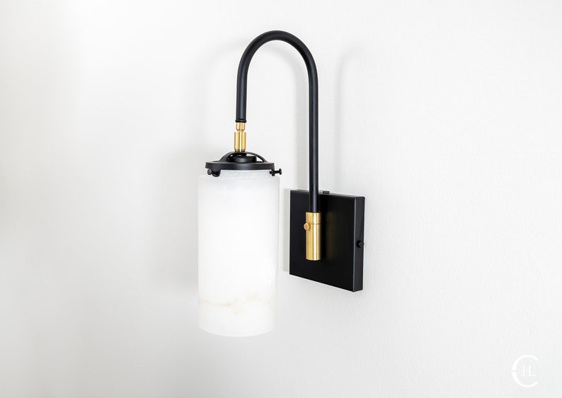 May include: Black wall sconce with a white alabaster glass shade and gold accents. The sconce has a curved arm and a square base.