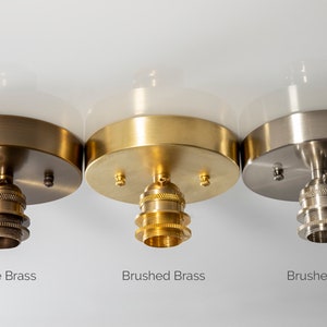 May include: Three ceiling light fixtures with white glass shades and different finishes: antique brass, brushed brass, and brushed nickel. Each fixture has a standard light bulb socket.
