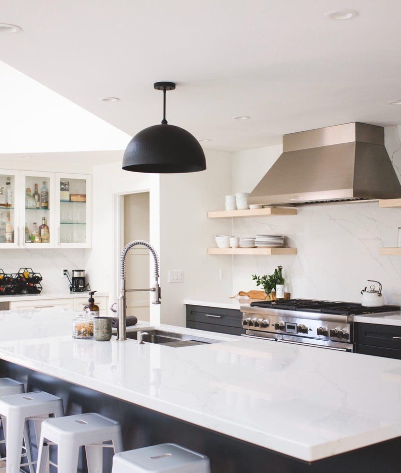 May include: A modern kitchen with white cabinets, a white countertop, and a black pendant light. The kitchen features a stainless steel range hood, a farmhouse sink, and a white quartz countertop.
