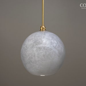May include: A white, round pendant light with a textured, paper-like finish. The light is suspended from a gold cord and has a gold metal fixture.