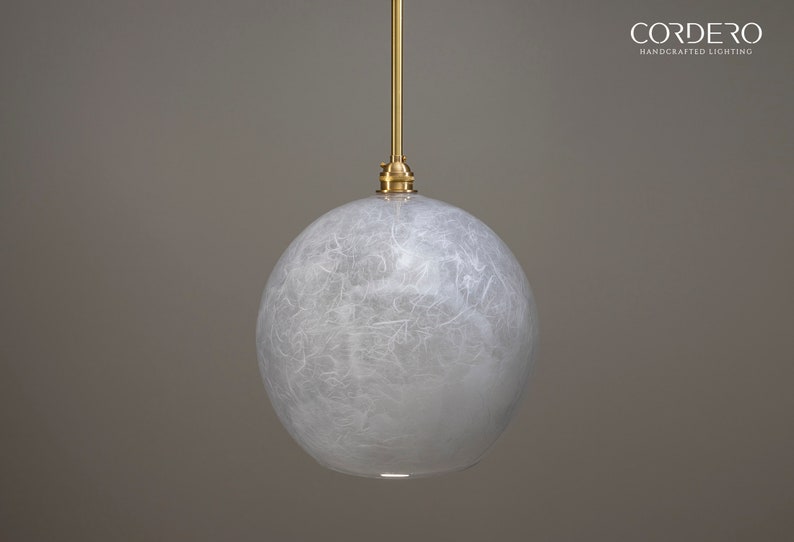 May include: A white, round pendant light with a textured, paper-like finish. The light is suspended from a gold cord and has a gold metal fixture.