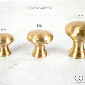 May include: Three satin brass finish cabinet knobs in varying sizes, labeled AA, BB, and CC. Each knob features a hammered texture on the rounded top and a cylindrical base. The text "3 Sizes Available" is above the knobs, and the Cordero Handcrafted Lighting logo is at the bottom.