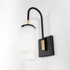 May include: A black wall sconce with a frosted glass shade and gold accents. The sconce has a curved arm and a square base.