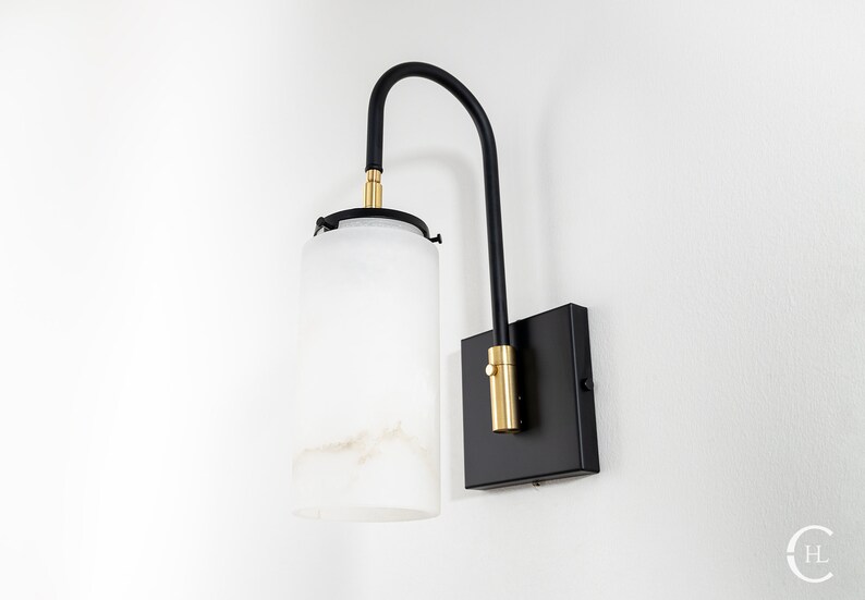 May include: A black wall sconce with a frosted glass shade and gold accents. The sconce has a curved arm and a square base.