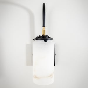 May include: A black wall sconce with a white alabaster glass shade. The sconce has a curved arm and a brass accent.