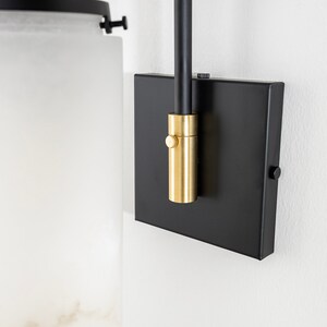 May include: Black wall sconce with a frosted glass shade and a gold-toned switch. The sconce has a black metal arm and a square base.