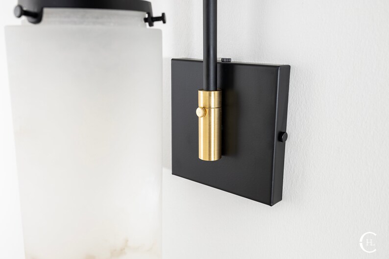 May include: Black wall sconce with a frosted glass shade and a gold-toned switch. The sconce has a black metal arm and a square base.