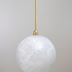 May include: A white globe pendant light with a gold metal cord and a white textured glass shade. The light is hanging from a ceiling.
