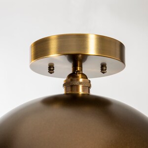 May include: A brass ceiling light fixture with a dome-shaped shade and a round ceiling plate. The fixture has a simple design and a brushed brass finish.