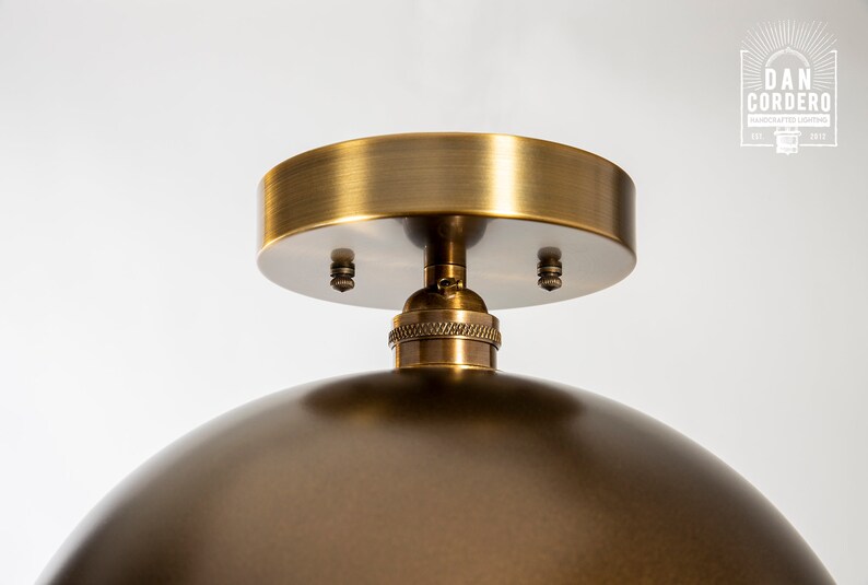 May include: A brass ceiling light fixture with a dome-shaped shade and a round ceiling plate. The fixture has a simple design and a brushed brass finish.