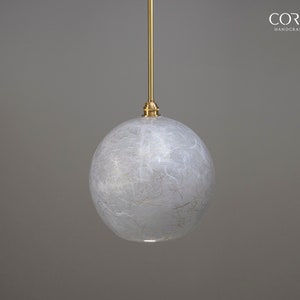 May include: A white, round, textured glass pendant light fixture with a gold metal hanging rod. The light fixture is suspended from the ceiling.