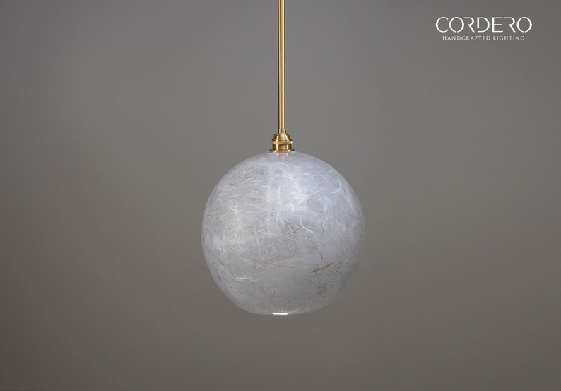 May include: A white, round, textured glass pendant light fixture with a gold metal hanging rod. The light fixture is suspended from the ceiling.