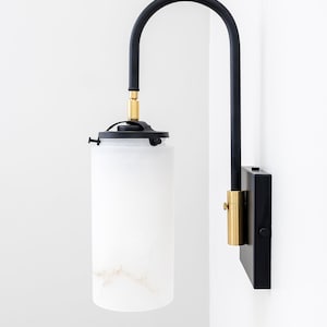 May include: A black and gold wall sconce with a white alabaster shade. The sconce has a curved arm and a square base.