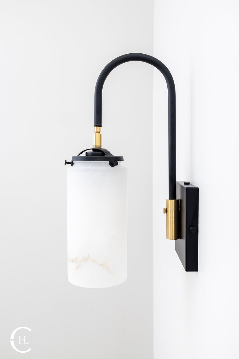May include: A black and gold wall sconce with a white alabaster shade. The sconce has a curved arm and a square base.