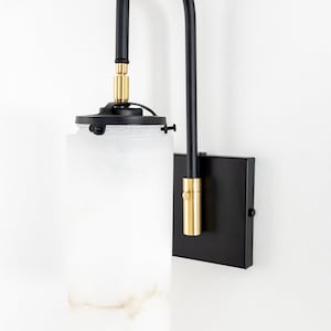 May include: A black wall sconce with a frosted glass shade and gold accents. The sconce has a curved arm and a square base.