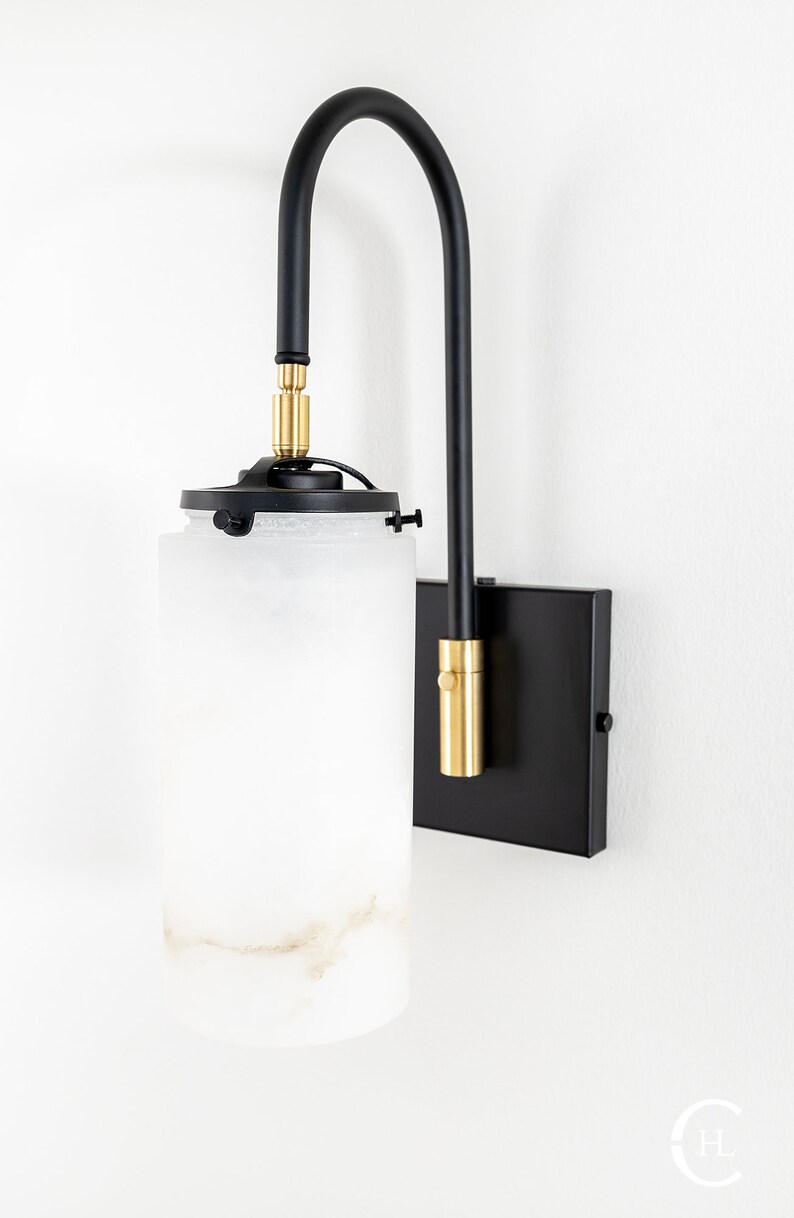 May include: A black wall sconce with a frosted glass shade and gold accents. The sconce has a curved arm and a square base.