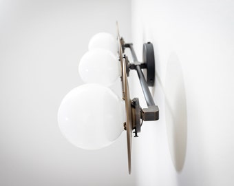 May include: A black metal wall-mounted light fixture with four white globe-shaped light bulbs. The fixture has a brushed brass finish and a modern design.