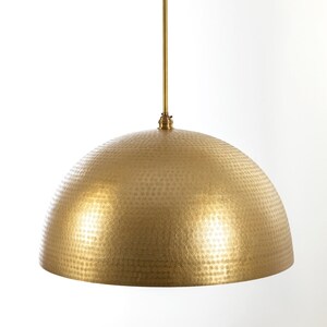 May include: A gold hammered metal dome pendant light fixture with a long, straight rod hanging from the ceiling.  CORDERO HANDCRAFTED LIGHTING is printed in black text at the top of the image.