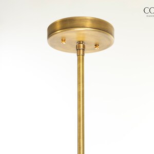 May include: A gold metal ceiling plate with two screw holes and a matching gold metal rod extending downwards.  CORDERO HANDCRAFTED LIGHTING is printed in black text on a white background.