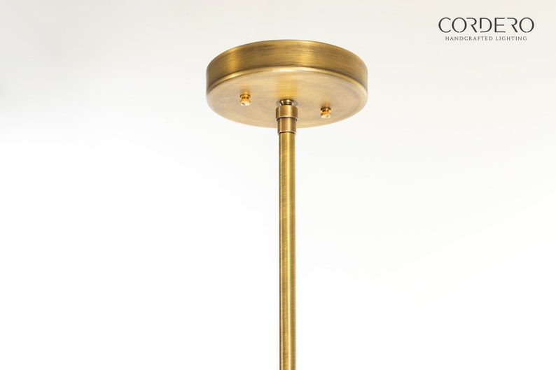 May include: A gold metal ceiling plate with two screw holes and a matching gold metal rod extending downwards.  CORDERO HANDCRAFTED LIGHTING is printed in black text on a white background.