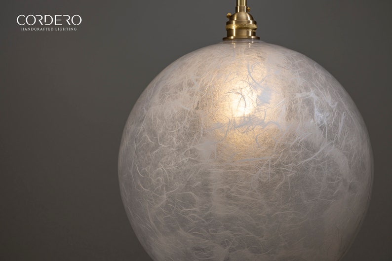May include: A white, round, glass pendant light fixture with a textured, paper-like surface. The light fixture is suspended from a brass cord.