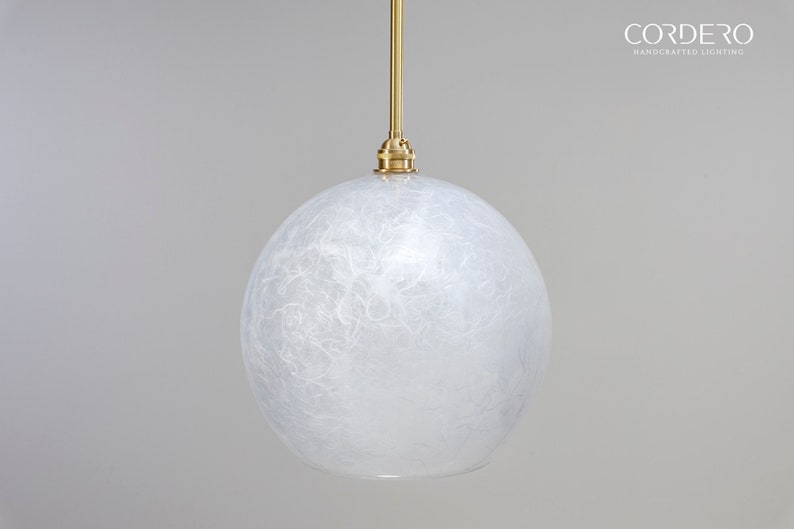 May include: A white, round, textured glass pendant light fixture with a brass hanging rod and a brass ceiling mount. The light fixture is hanging from a white ceiling.