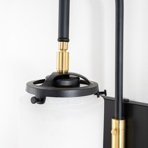 May include: Black and gold wall sconce with a frosted glass shade. The sconce has a swivel arm and a round base.