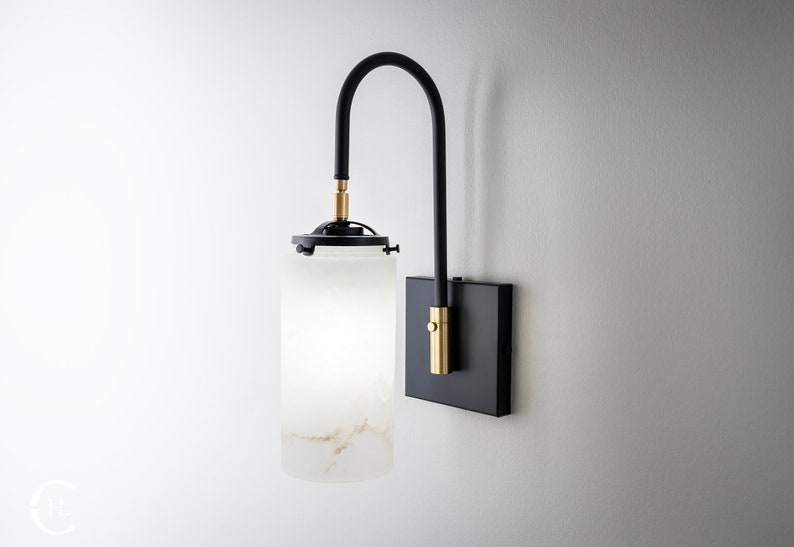 May include: A black wall-mounted light fixture with a curved arm and a frosted glass shade. The shade has a white and gold marbled pattern. The fixture has a brass accent on the arm.
