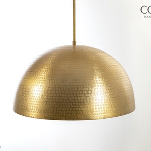May include: A gold, hammered metal pendant light fixture with a dome-shaped shade. The shade has a textured surface with a pattern of small circles.