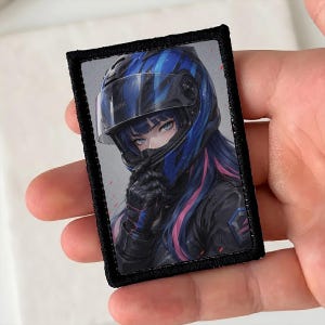Pode incluir: Um emblema retangular bordado com uma ilustração estilo anime de uma pessoa usando um capacete de moto azul e preto com viseira transparente, uma jaqueta de couro preta e luvas pretas, com cabelos azuis e rosas visíveis.