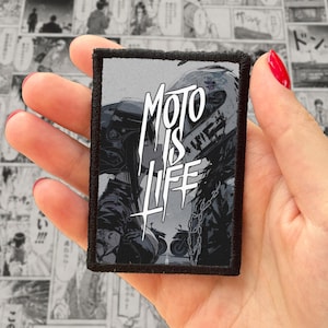 Könnte beinhalten: Ein rechteckiger bestickter Aufnäher mit schwarzem Rand zeigt eine graustufige Manga-Illustration von zwei Personen mit Motorradhelmen. Der Text MOTO IS LIFE ist in einer fetten, weißen, stilisierten Schrift in der Mitte des Bildes gedruckt.