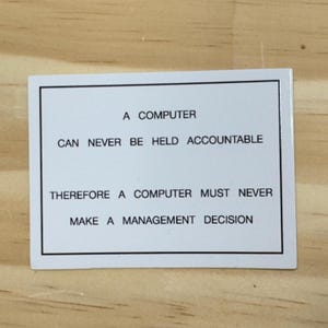 May include: A rectangular white sticker featuring a thin black border and black text that reads: A COMPUTER CAN NEVER BE HELD ACCOUNTABLE THEREFORE A COMPUTER MUST NEVER MAKE A MANAGEMENT DECISION. The sticker has a smooth, clean finish.