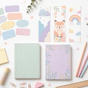 May include: A stationery set featuring two notebooks, one solid light green and one lavender with a leaf border, three bookmarks with fox, rainbow, and cloud illustrations, pastel sticky notes, colored pencils, paper clips, and a wooden ruler.